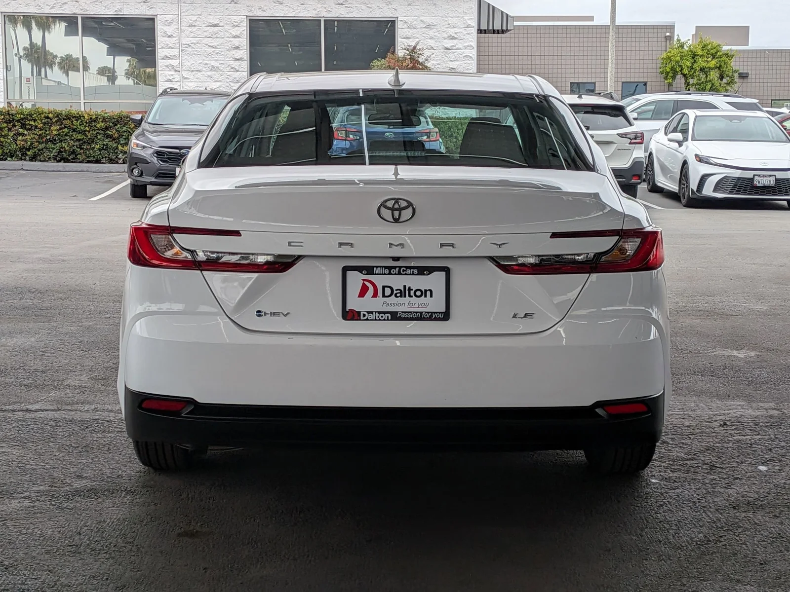 Rear view of a white used Toyota Camry LE HEV with the Dalton dealer plate