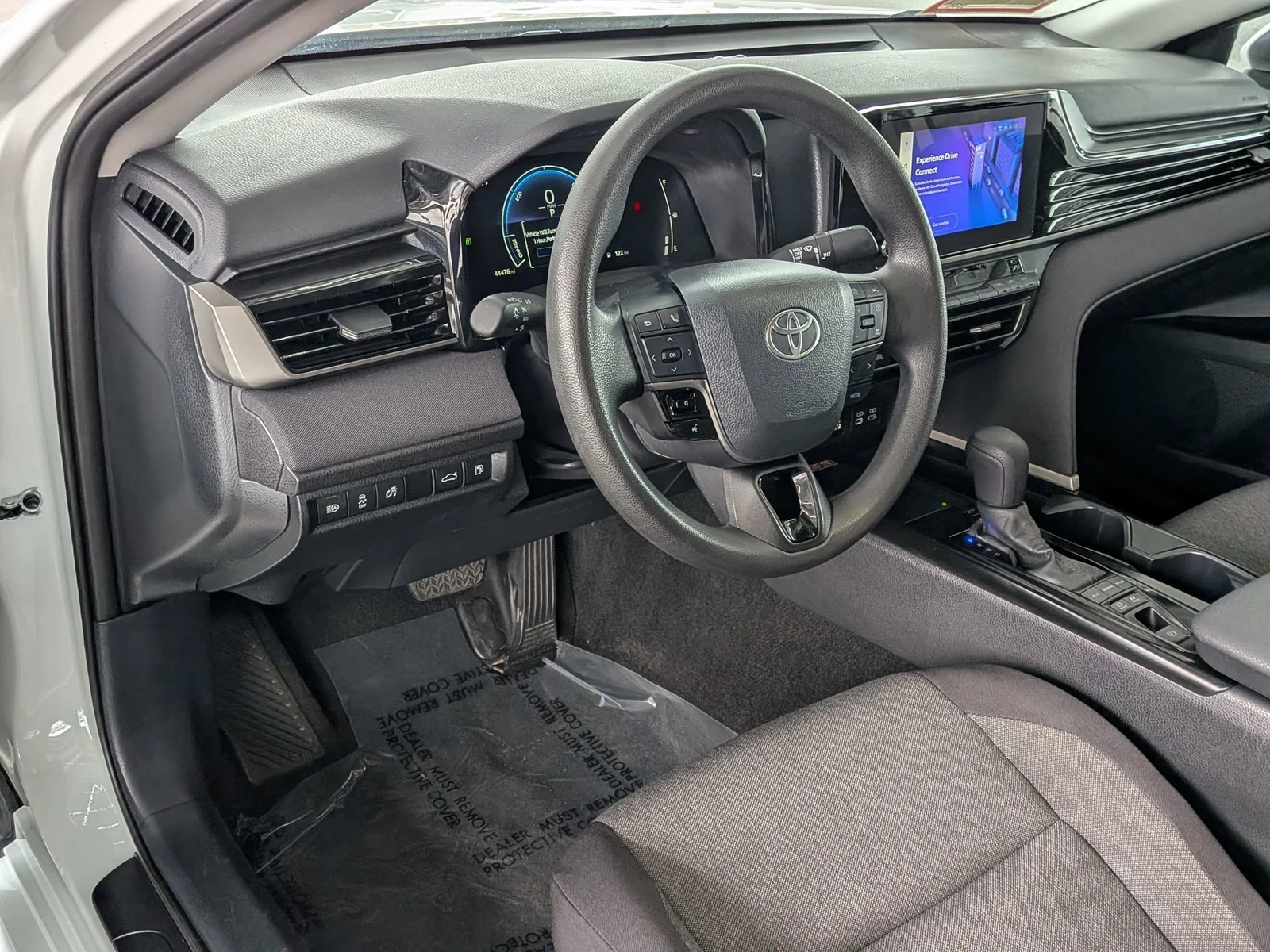 Driver's cockpit of a used Toyota Camry with digital gauges, touchscreen, and shifter