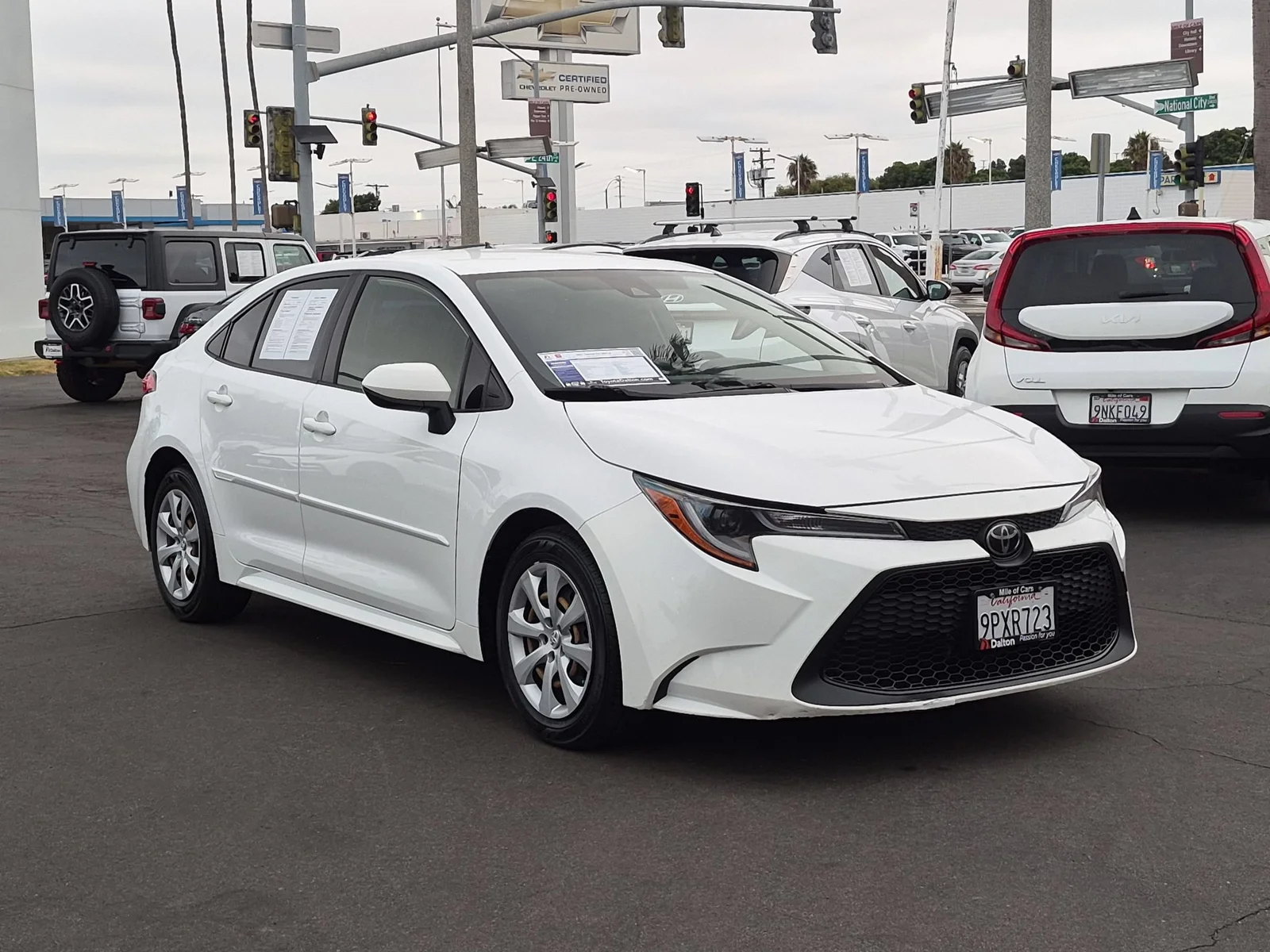 A white Toyota Corolla with its window sticker still in place, parked on the used-car front line at Dalton Toyota National City
